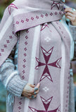 A close-up of a person wearing a dusty grey geometric patterned knit wool scarf with dark purple geometric stars, standing outdoors in a green forest