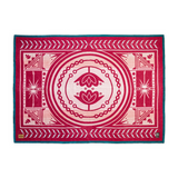 A woven wool blanket featuring a symmetrical mandala design in magenta and cream with a teal border, shown flat against a white background.