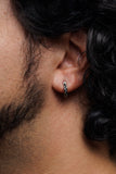 A close-up side view of a person's ear wearing a small silver huggie hoop earring with a textured, beaded outer edge.