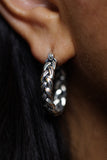 A close-up of a person's ear wearing a thick braided silver hoop earring.