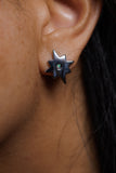 A close-up of a person's ear wearing a dark metallic star-shaped stud earring with a small green stone in the center.