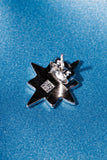 A close-up of a silver star-shaped earring back with a black center, resting on a textured blue fabric background.