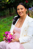 Woman in a white blazer and pink dress holding flowers outdoors