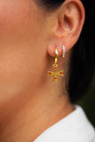Close-up of a person wearing gold cross earrings with red stones.