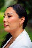 Woman wearing gold earrings with a blurred green background