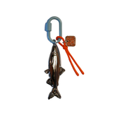 A metal fish-shaped keychain charm with an attached blue carabiner, orange cord, and small square copper tag on a plain white background.