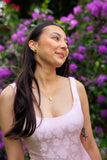 Woman in a light pink sleeveless top standing in front of purple flowers